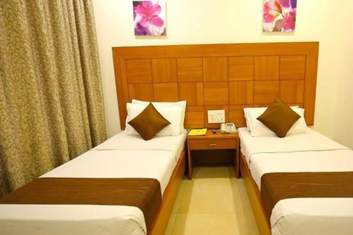A hotel room with two single beds, wooden headboards, white bedding, a nightstand with a telephone, and a curtain.