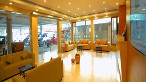 Un vestíbulo amplio con diseño moderno, que incluye una zona de estar con sofás y una mesa de centro, y grandes ventanales con vistas a coches estacionados afuera.
