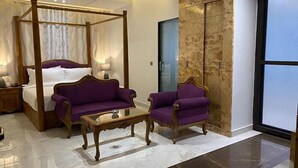 A bedroom with a four-poster bed, two purple armchairs, and a small wooden table. - Fabhotel Prime The Daffodils (Dehradun)