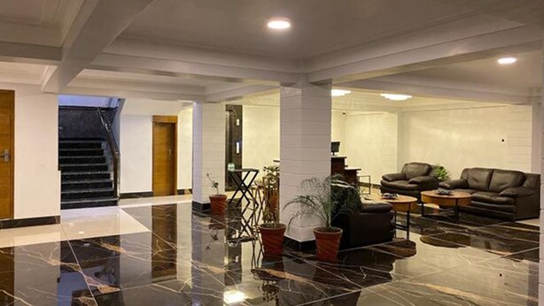 A spacious lobby with a marble floor, a leather sofa, a coffee table, and a potted plant. - Fabhotel Prime The Daffodils (Dehradun)