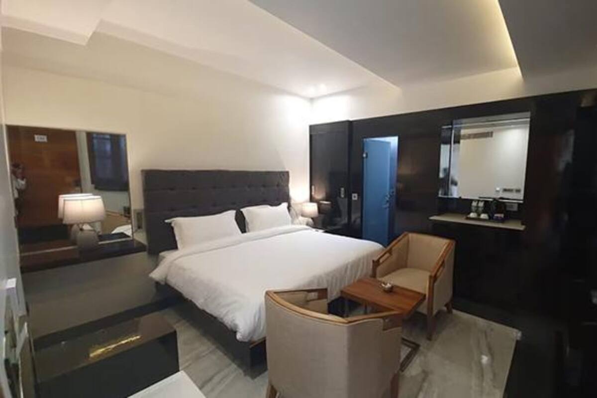 Quarto de hotel com uma cama grande, uma escrivaninha, uma cadeira, um espelho e um guarda-roupa.
