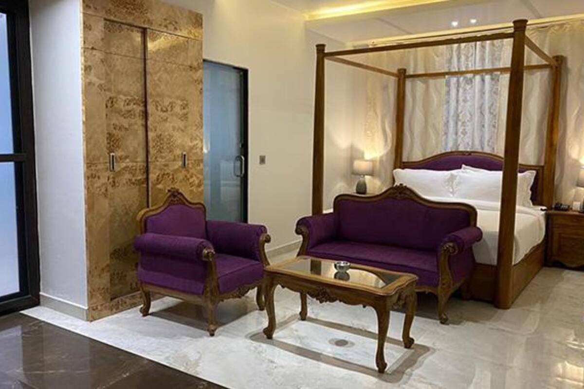 Quarto com cama de dossel, duas poltronas roxas, mesa de centro de madeira e um guarda-roupa grande com espelho.