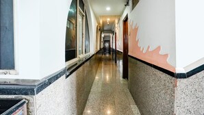 A long, narrow hallway with a polished floor, arched windows on one side, and a wall with a decorative pattern on the other. - Fabhotel Silver Inn Ii (Nashik)