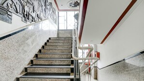 A marble staircase with metal railings, leading to a landing with a red emergency exit sign. - Fabhotel Silver Inn Ii (Nashik)