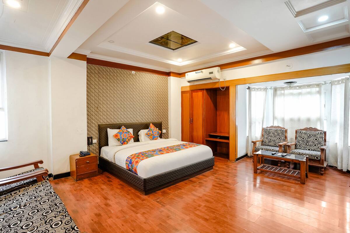 A hotel room with a large bed, wooden wardrobe, two armchairs, a small table, and a ceiling fan.
