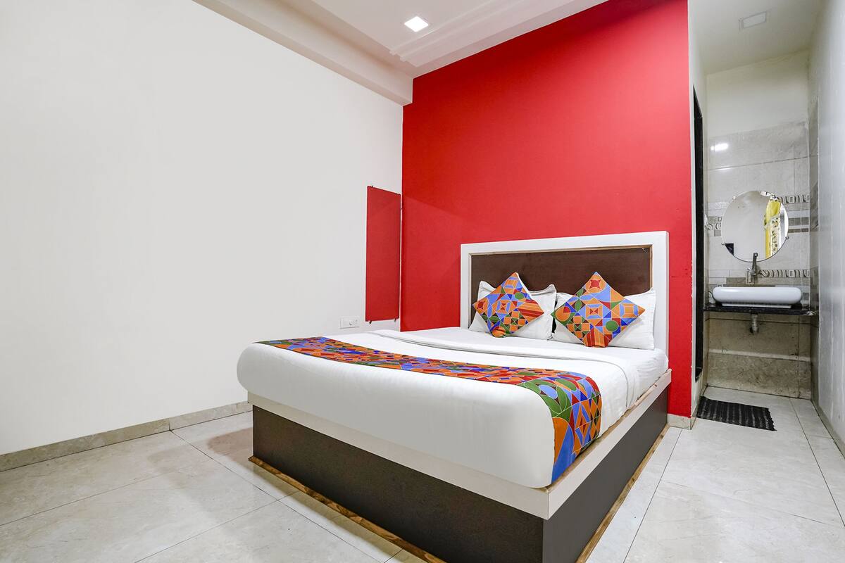Quarto moderno com cama grande, parede de destaque vermelha e banheiro com pia e espelho brancos.