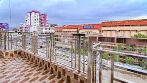 En balkon med et mønstret gulv, der kigger ud over en gade med bygninger, heriblandt en skole.
