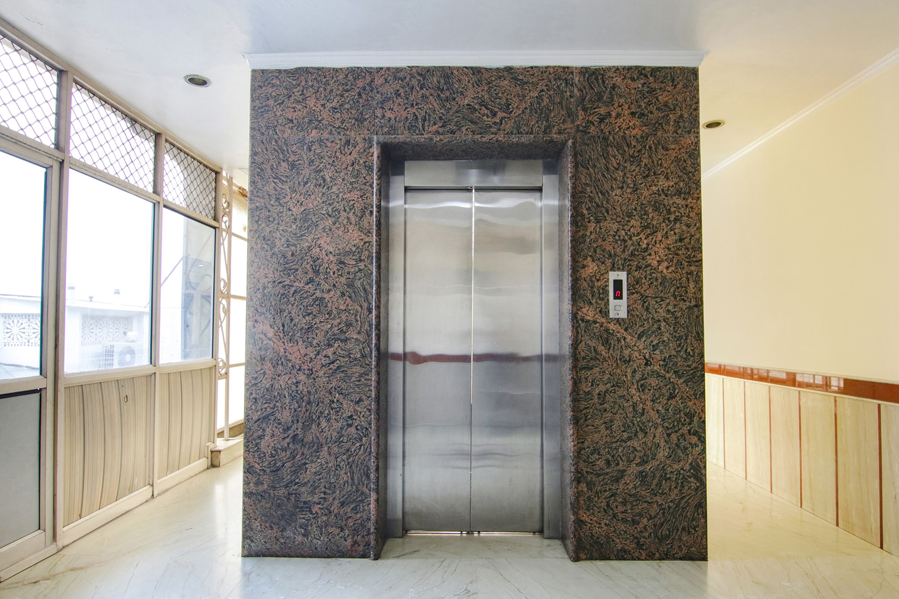 An elevator in a hallway with a marble wall and wooden paneling.
