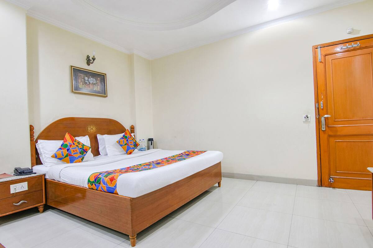 A neatly made bed with a colorful quilt, a wooden headboard, and a nightstand with a phone.