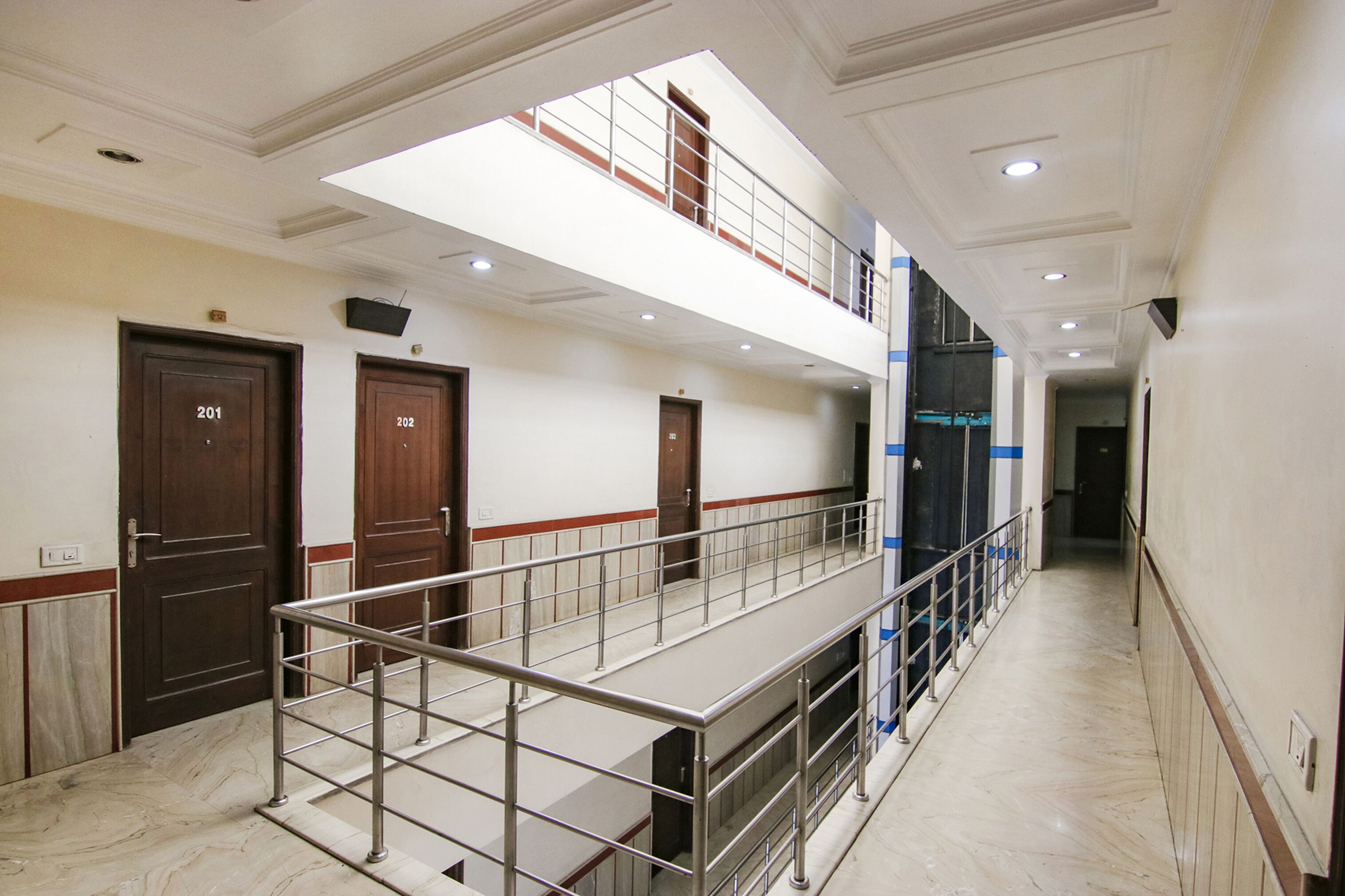 A multi-level hotel corridor with marble flooring, metal railings, and doors numbered 201 and 202.