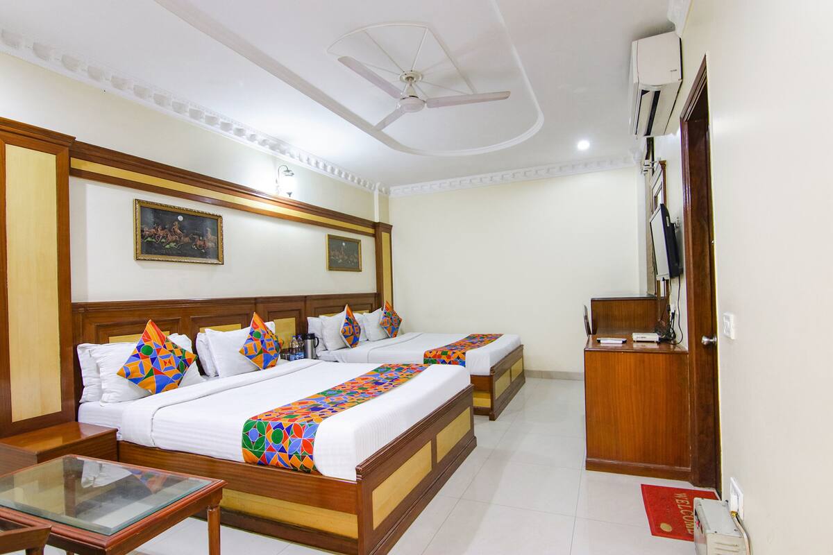 A hotel room with two beds, a desk, a chair, a ceiling fan, an air conditioning unit, and a television.