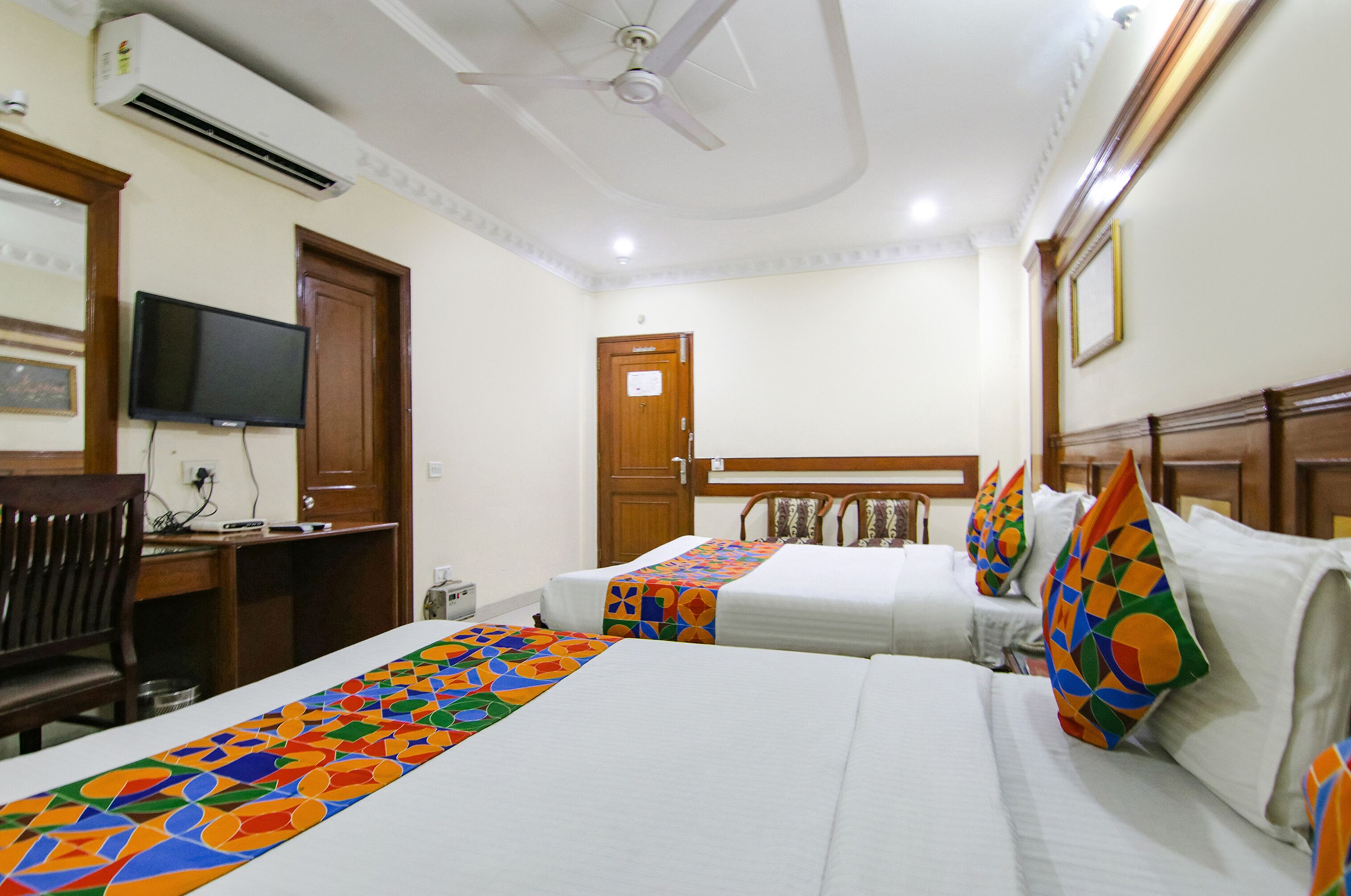 A hotel room with two beds, a television, a desk, and an air conditioning unit.