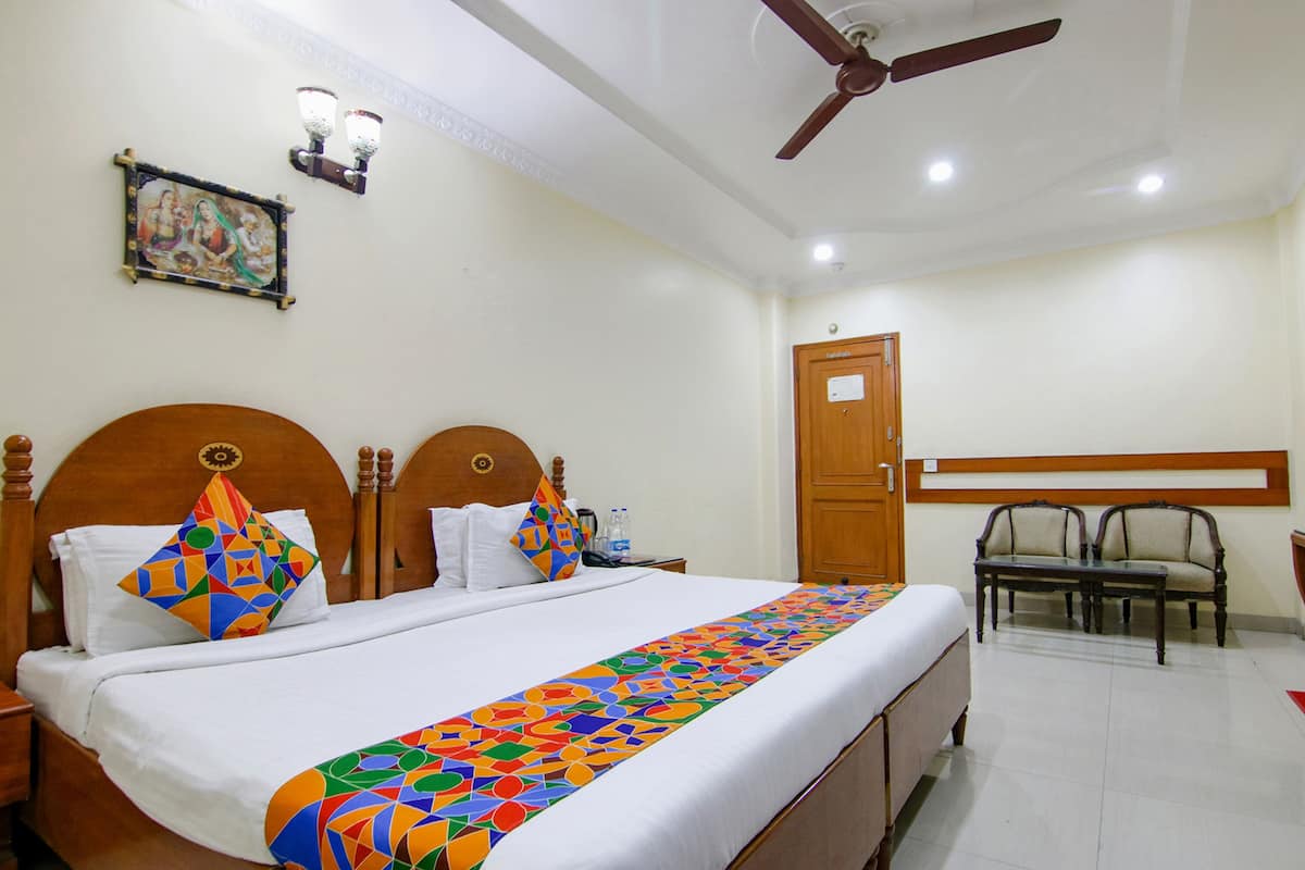 A hotel room with a large bed, two nightstands, a wooden headboard, a ceiling fan, a wall-mounted light fixture, a door, and two chairs.