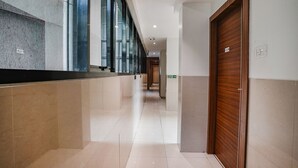 A corridor with a tiled floor, a wooden door on the right, and a glass wall on the left. - Fabhotel Konar Inn (Navi Mumbai)