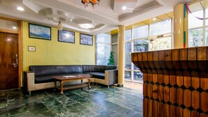 Un vestíbulo con un sofá de cuero negro, una mesa de centro de madera, un mostrador de recepción de madera y un árbol de Navidad verde.