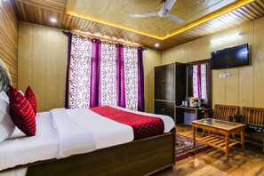 Quarto de hotel com cama, televisão, mesa de madeira e área de estar.