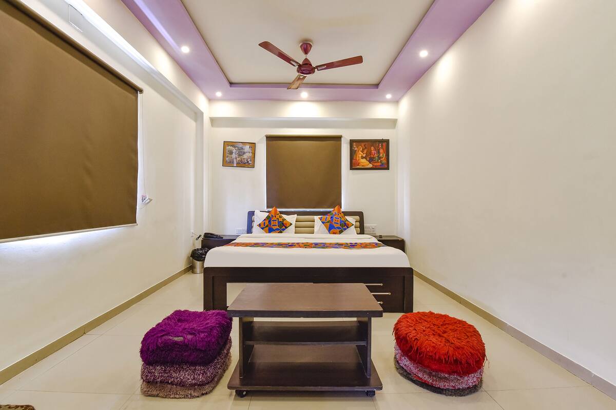 A bedroom with a bed, a ceiling fan, a nightstand, a bedside table, and two ottomans.