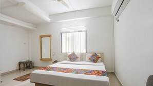 Una habitación de hotel con cama, mesita de noche, espejo, ventana con persianas y aire acondicionado.