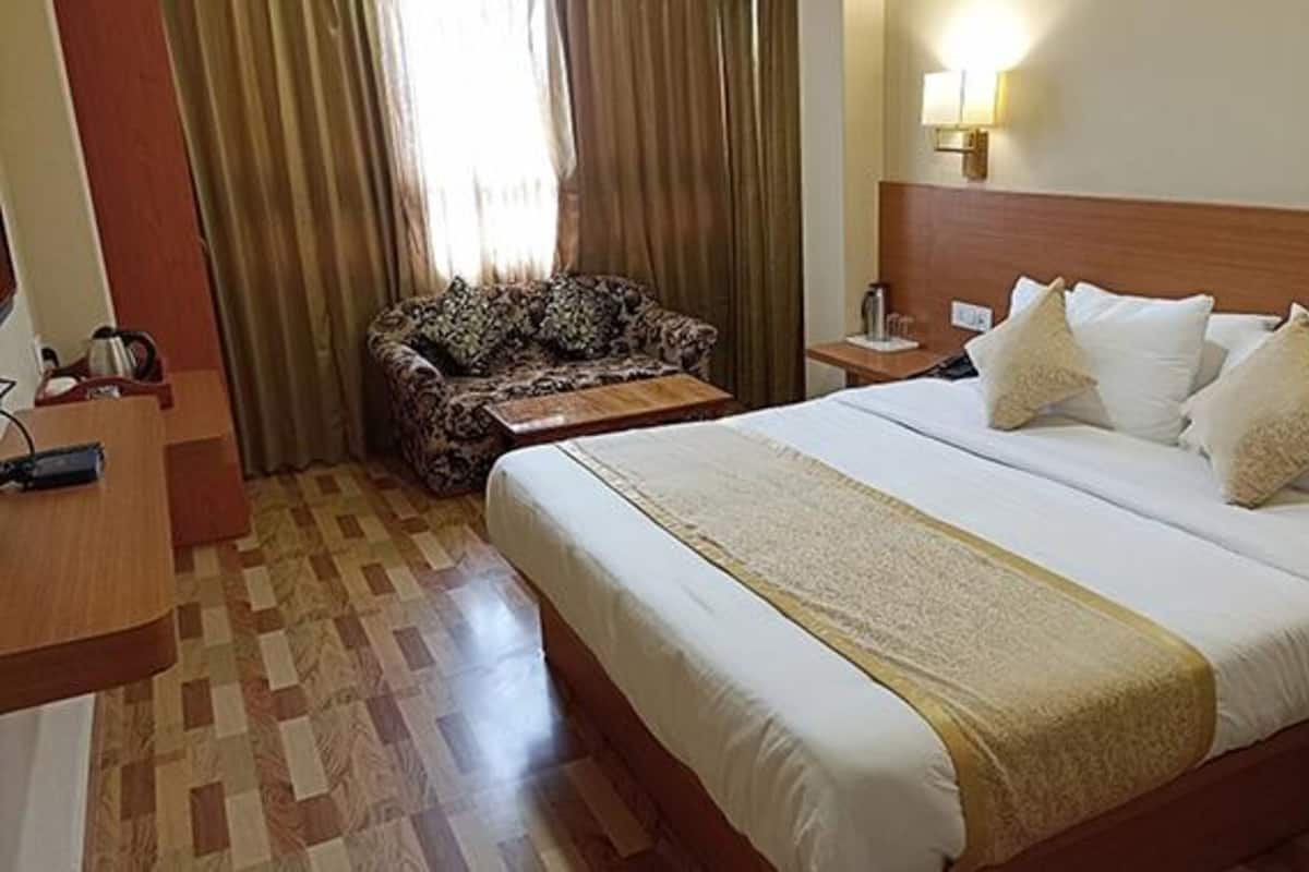 Une chambre d’hôtel avec un grand lit, une table de chevet en bois, un fauteuil à motifs et une fenêtre avec des rideaux.