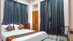 A hotel room with a bed, two pillows, a wooden wardrobe, and a chair. - Fabhotel Skyline I (Pune)