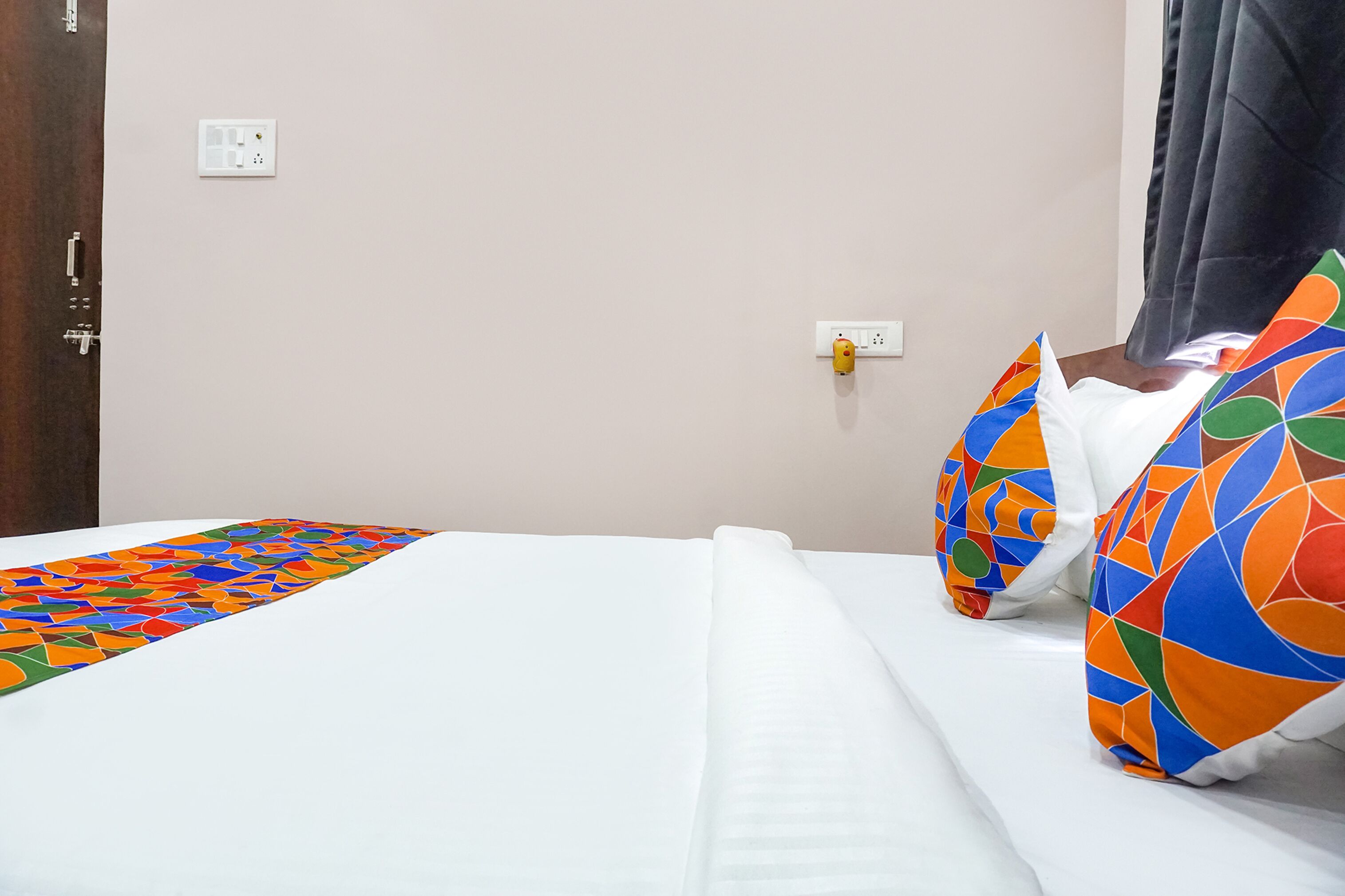 Una habitación de hotel con una cama, ropa de cama blanca, una manta de color y una almohada con diseño geométrico.