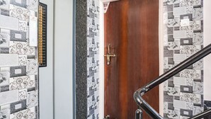 A wooden door with a brass handle, a vertical air conditioning unit, and a tiled wall with a floral pattern. - Fabhotel Skyline I (Pune)
