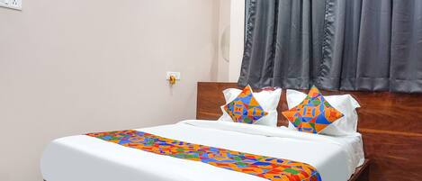 Una cama bien hecha con una colcha y almohadas de un colorido estampado geométrico, un cabecero de madera y una cortina gris.
