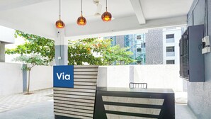 A reception desk with a 'Via' sign, a chair, hanging pendant lights, and a view of a building with scaffolding. - Fabhotel Skyline I (Pune)