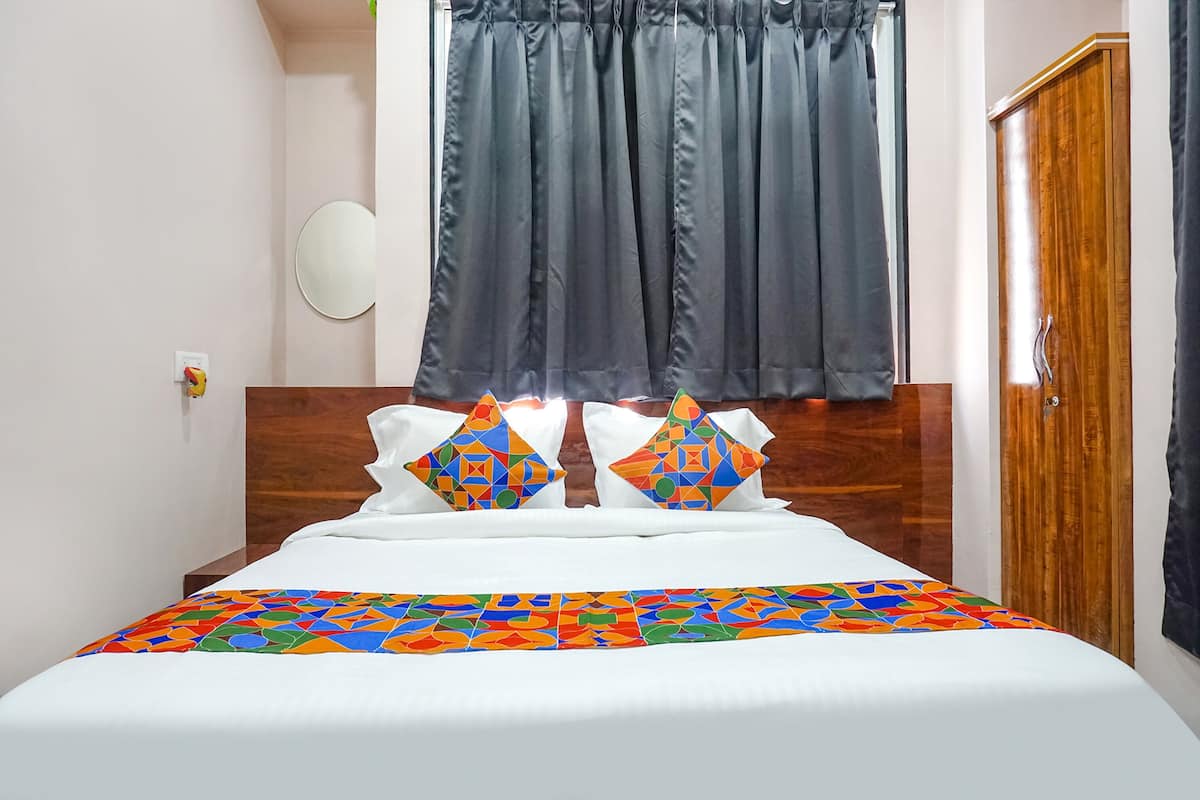 Una cama bien hecha con un edredón de estampado geométrico y colores vivos, dos almohadas decorativas y un cabecero de madera.