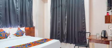 A hotel room with a bed, a chair, a table with a kettle, and curtains.