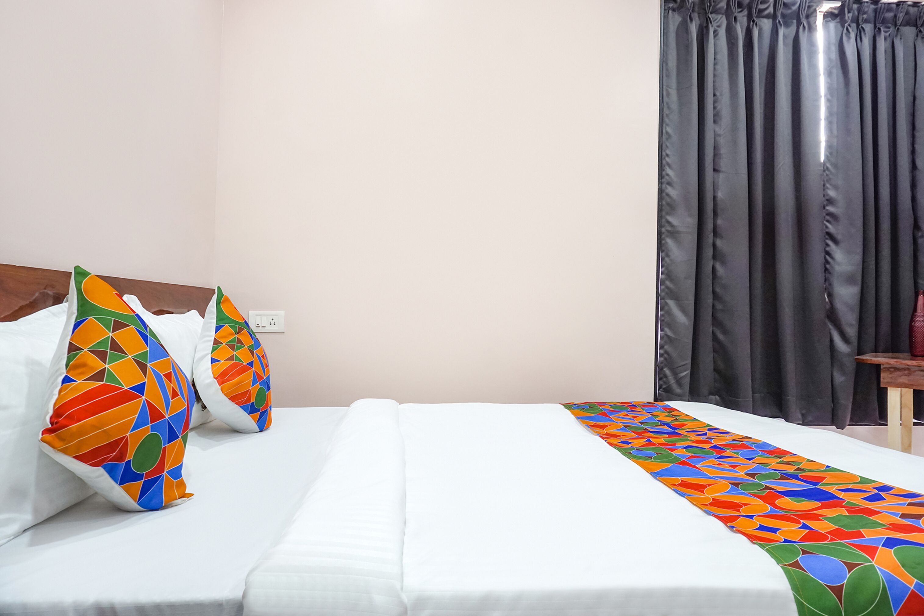 A neatly made bed with white linens and colorful geometric-patterned pillows.