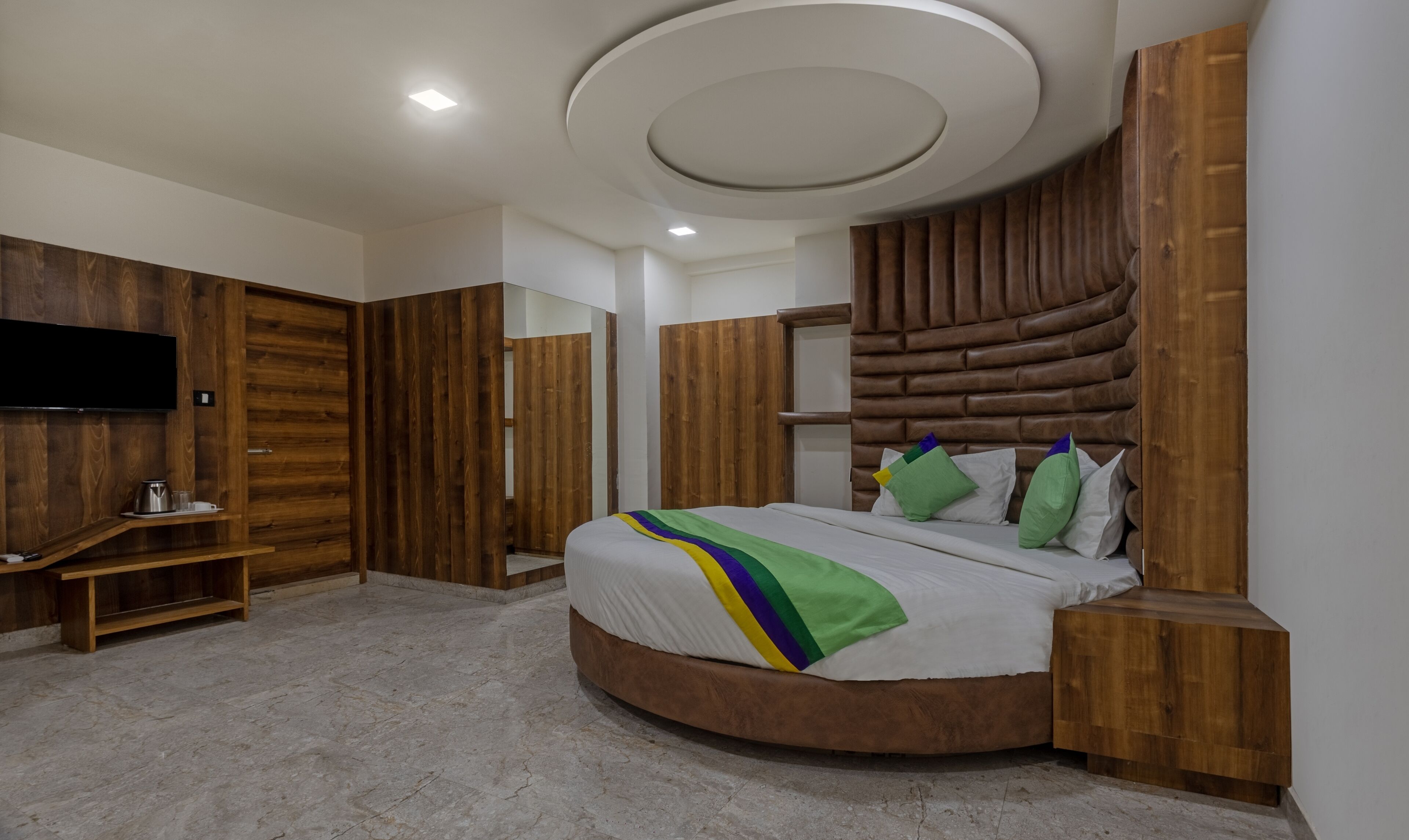 A modern bedroom with a curved bed, wooden panel walls, a flat-screen TV, and a built-in shelf.