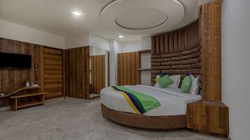 A modern bedroom with a curved bed, wooden panel walls, a flat-screen TV, and a built-in shelf.