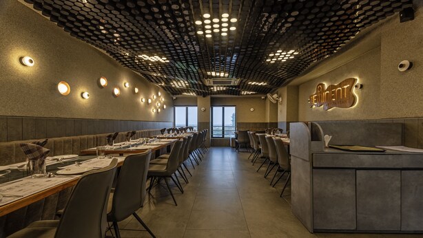 Een restaurant met een modern interieur, met een lange eettafel, meerdere stoelen en een balie.