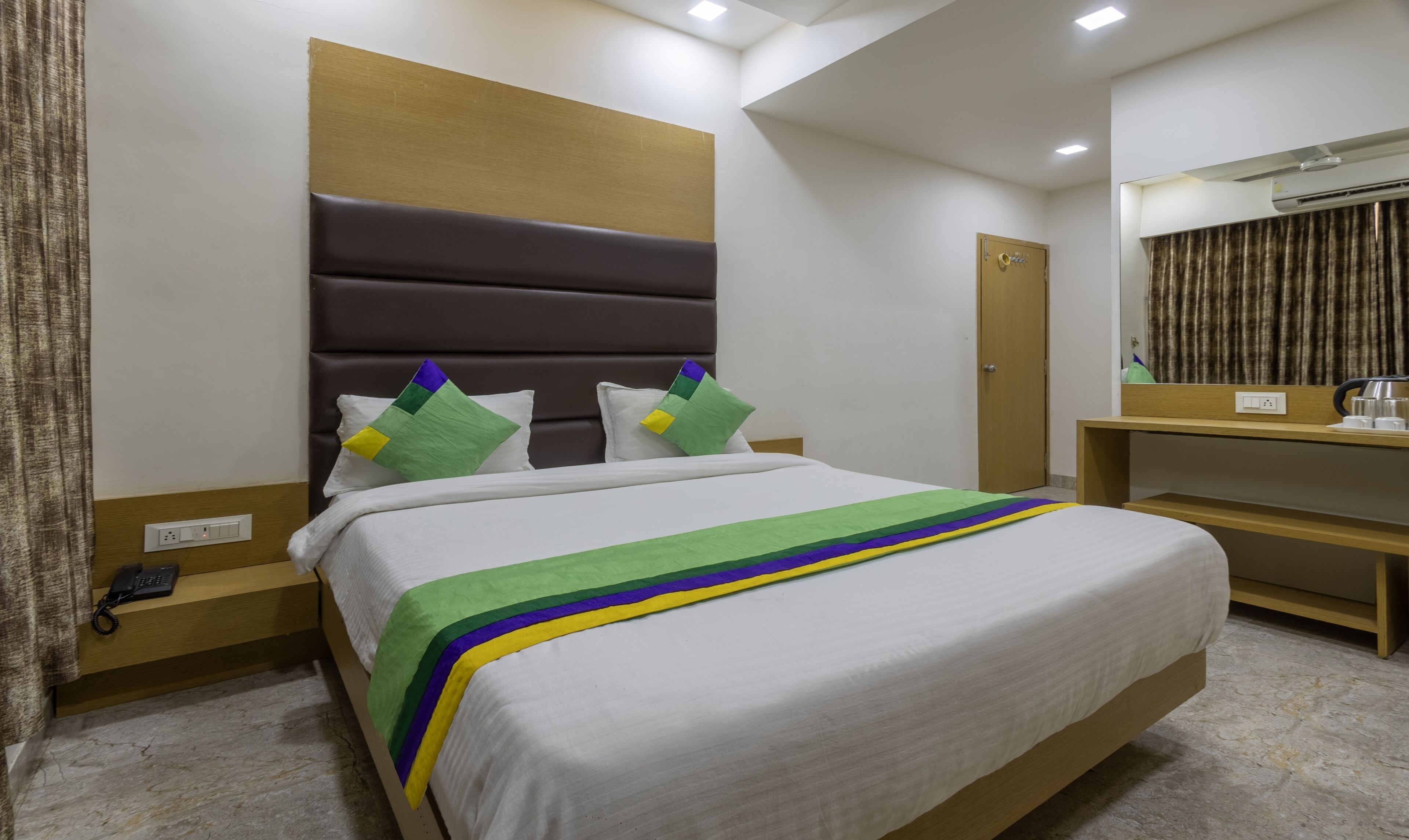A hotel room with a bed, a bedside table, a mirror, and a door.