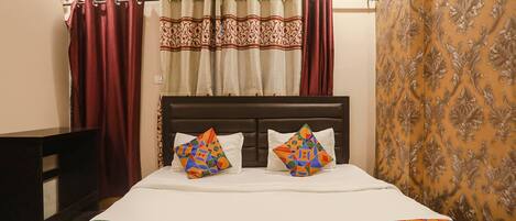 A bed with a patterned bedspread, two pillows, a headboard, and curtains.