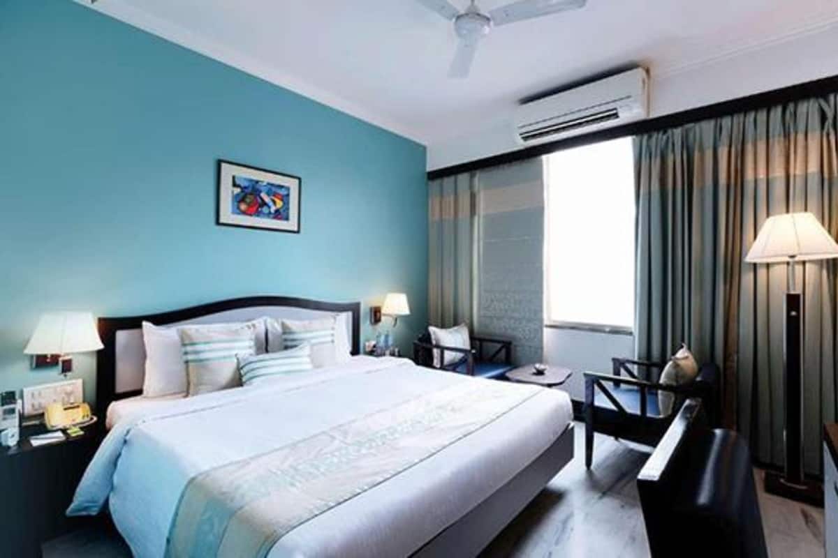A hotel room with a large bed, a desk, a chair, a desk lamp, a picture on the wall, and a window with curtains.