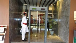 Entrada de un hotel con puerta de vidrio, un letrero que dice 'WALK' encima de la puerta, y un guardia de seguridad de pie afuera.
