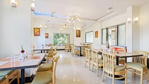 A spacious dining area with multiple tables and chairs, ceiling fans, and wall-mounted lights. - Fabhotel Prime Kb'S Grand (Rahata)