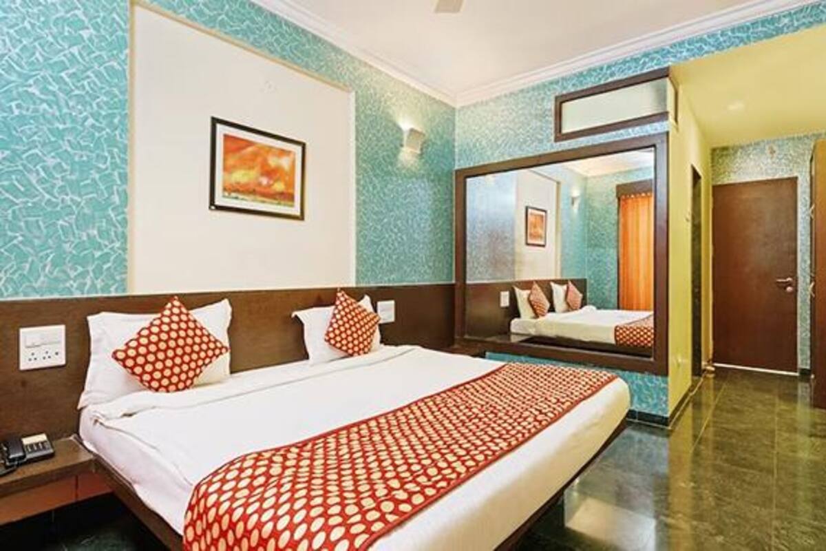 A hotel room with a bed, a nightstand, a mirror, and a door.