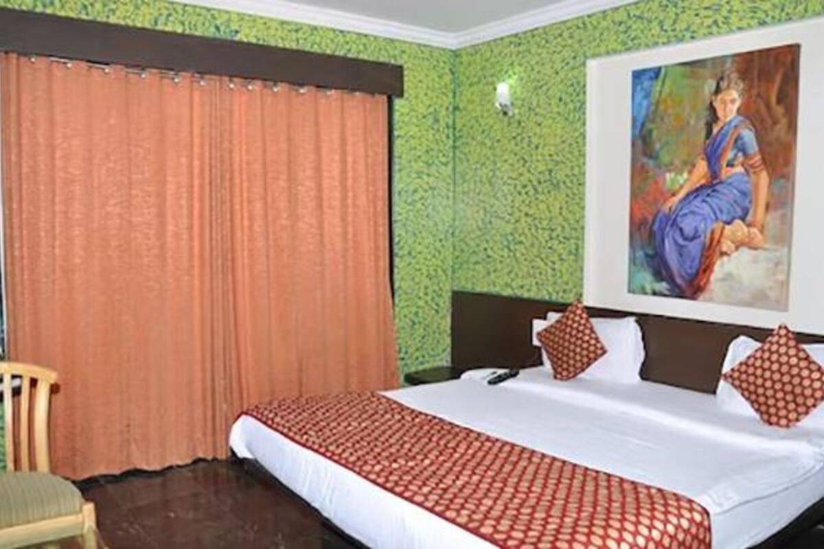 A hotel room with a large bed, a painting on the wall, and a window with curtains.