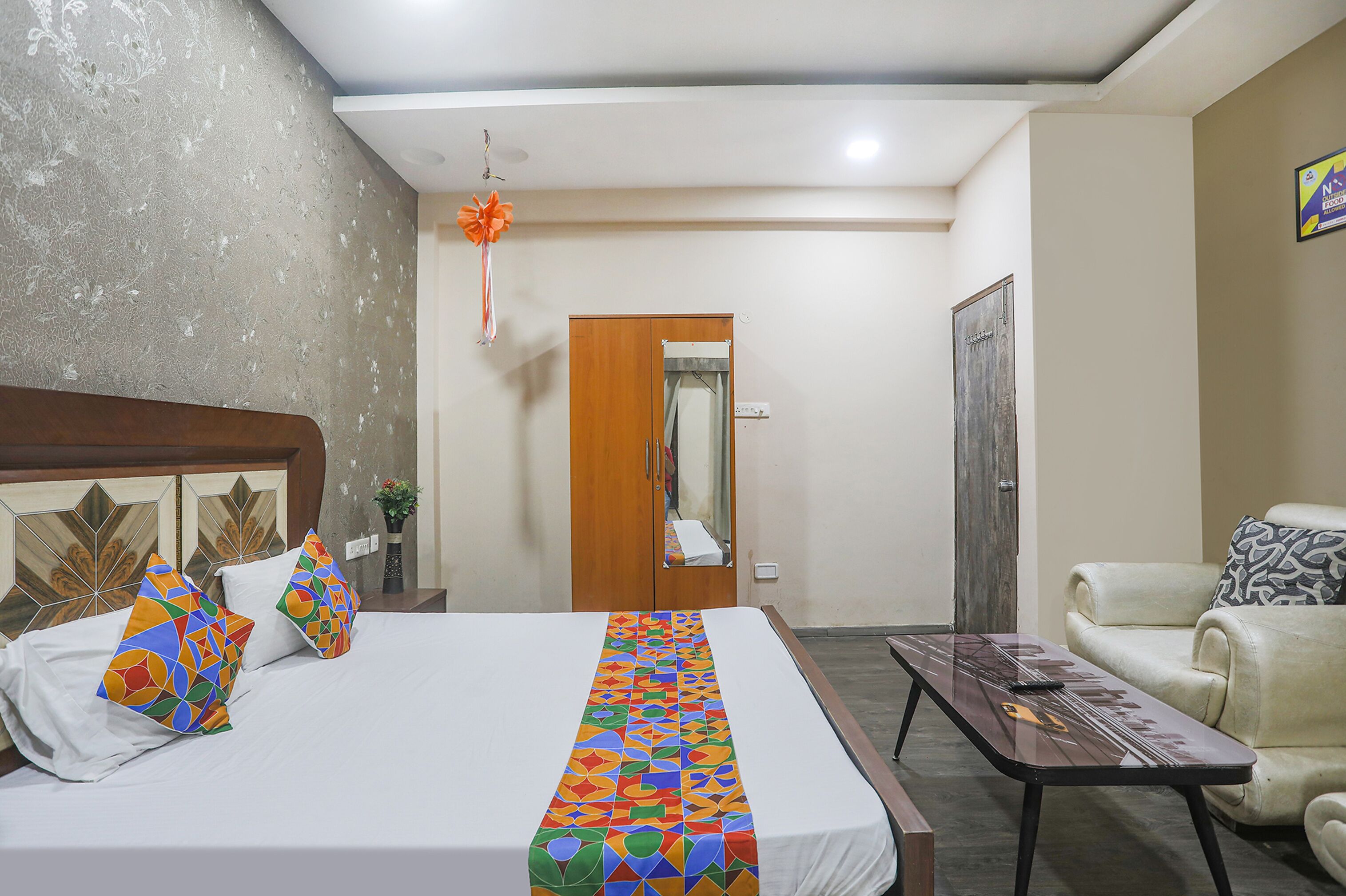 A hotel room with a bed, a wooden wardrobe, a small table, and a sofa.