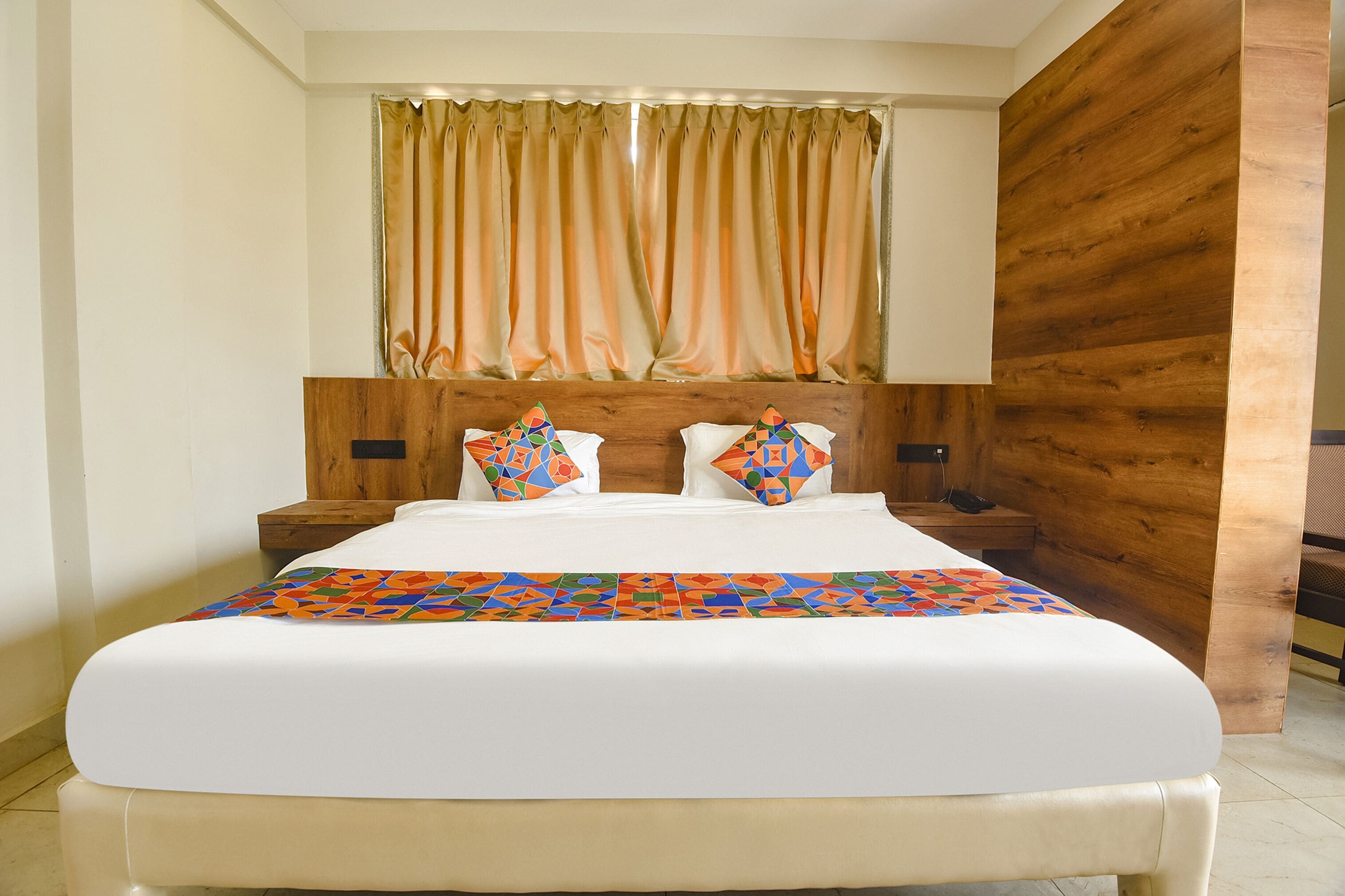 Quarto de hotel com uma cama grande, cabeceira de madeira e um edredom colorido.