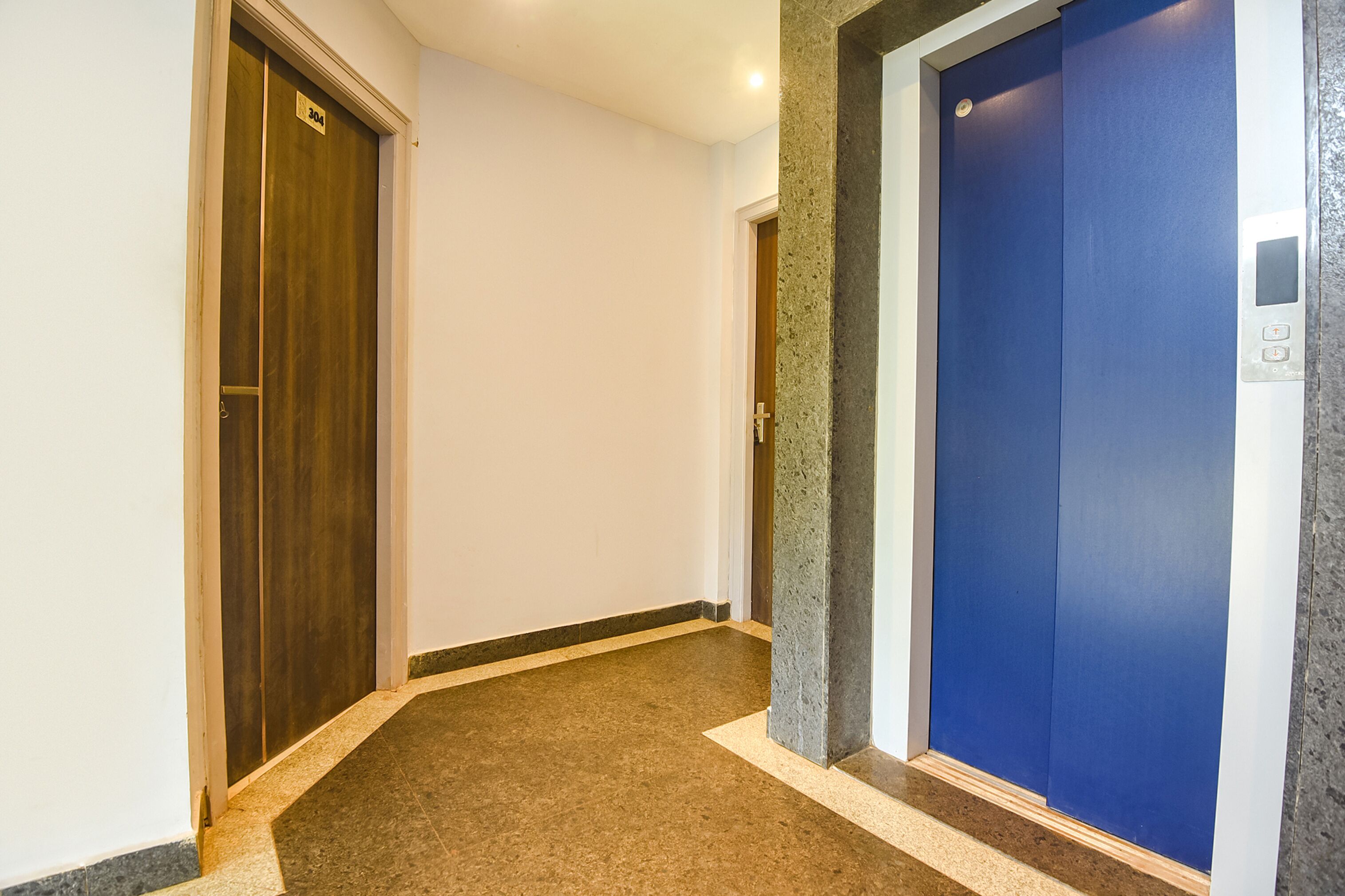 Um corredor com duas portas, uma delas com o número 304, que dá para um elevador com porta azul.