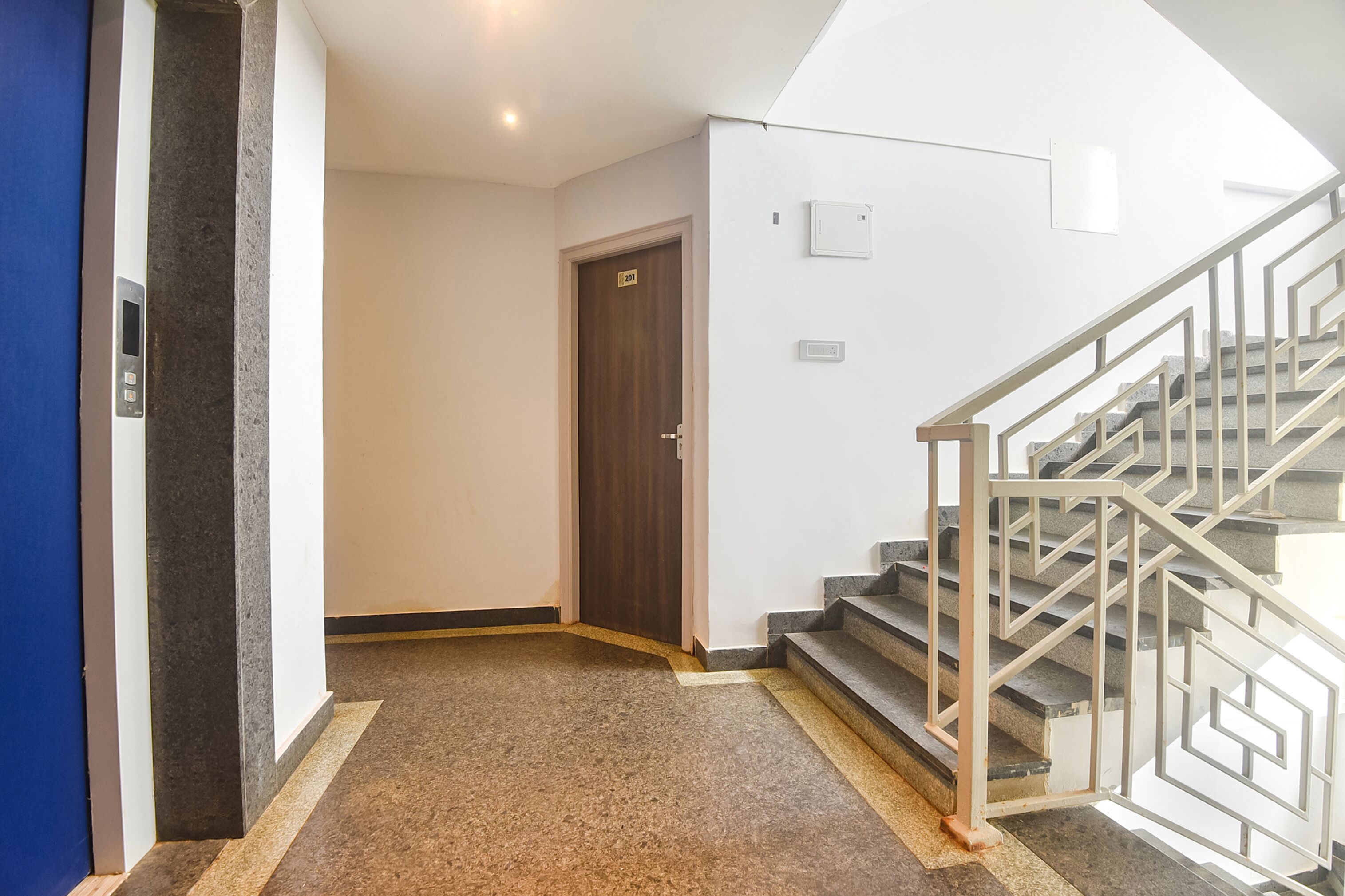 A hallway with a wooden door, a staircase with metal railings, and a carpeted floor.