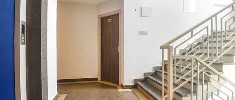A hallway with a wooden door, a staircase with metal railings, and a carpeted floor.