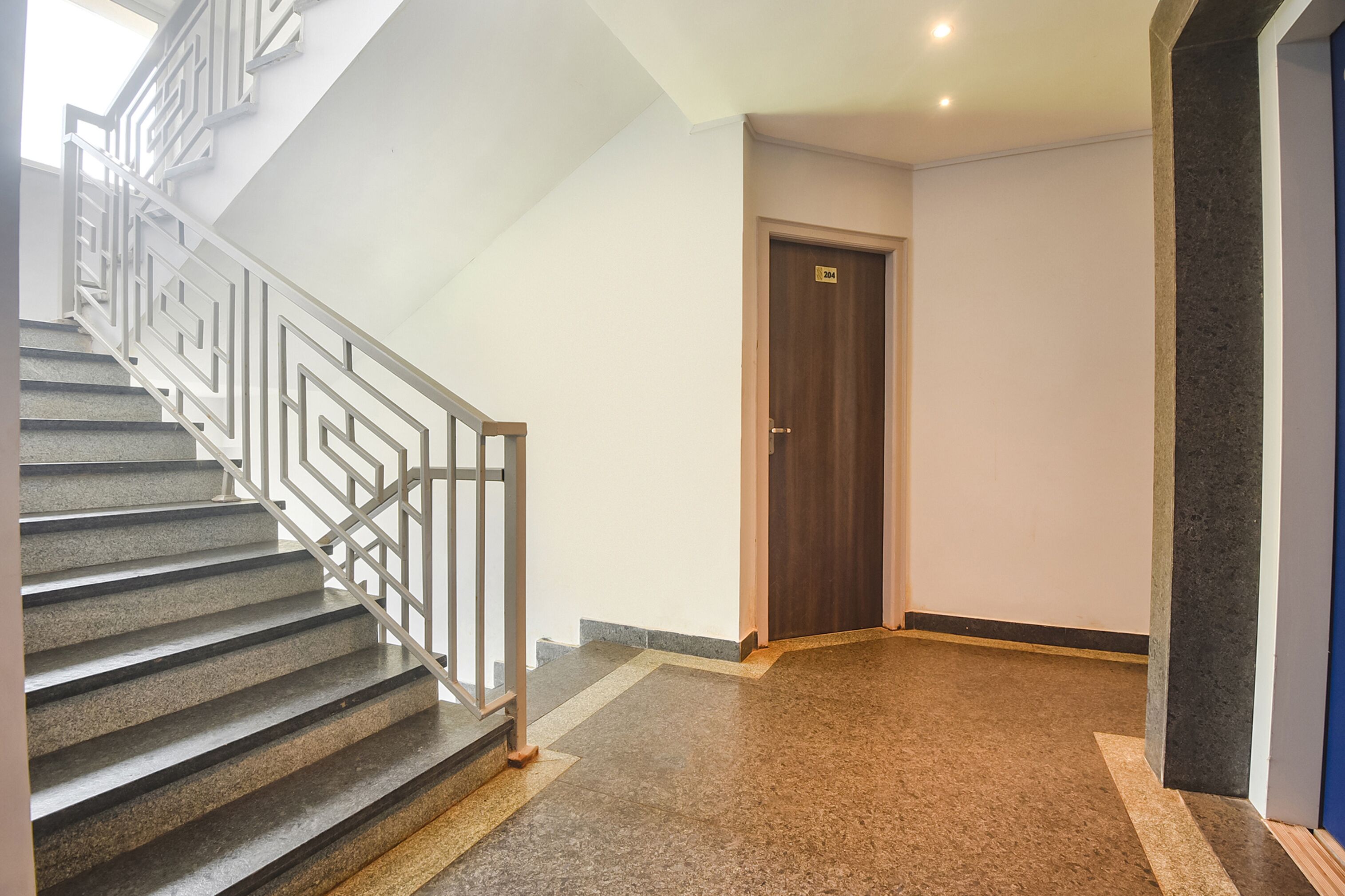 Una escalera con barandilla geométrica, una puerta de madera y piso alfombrado.