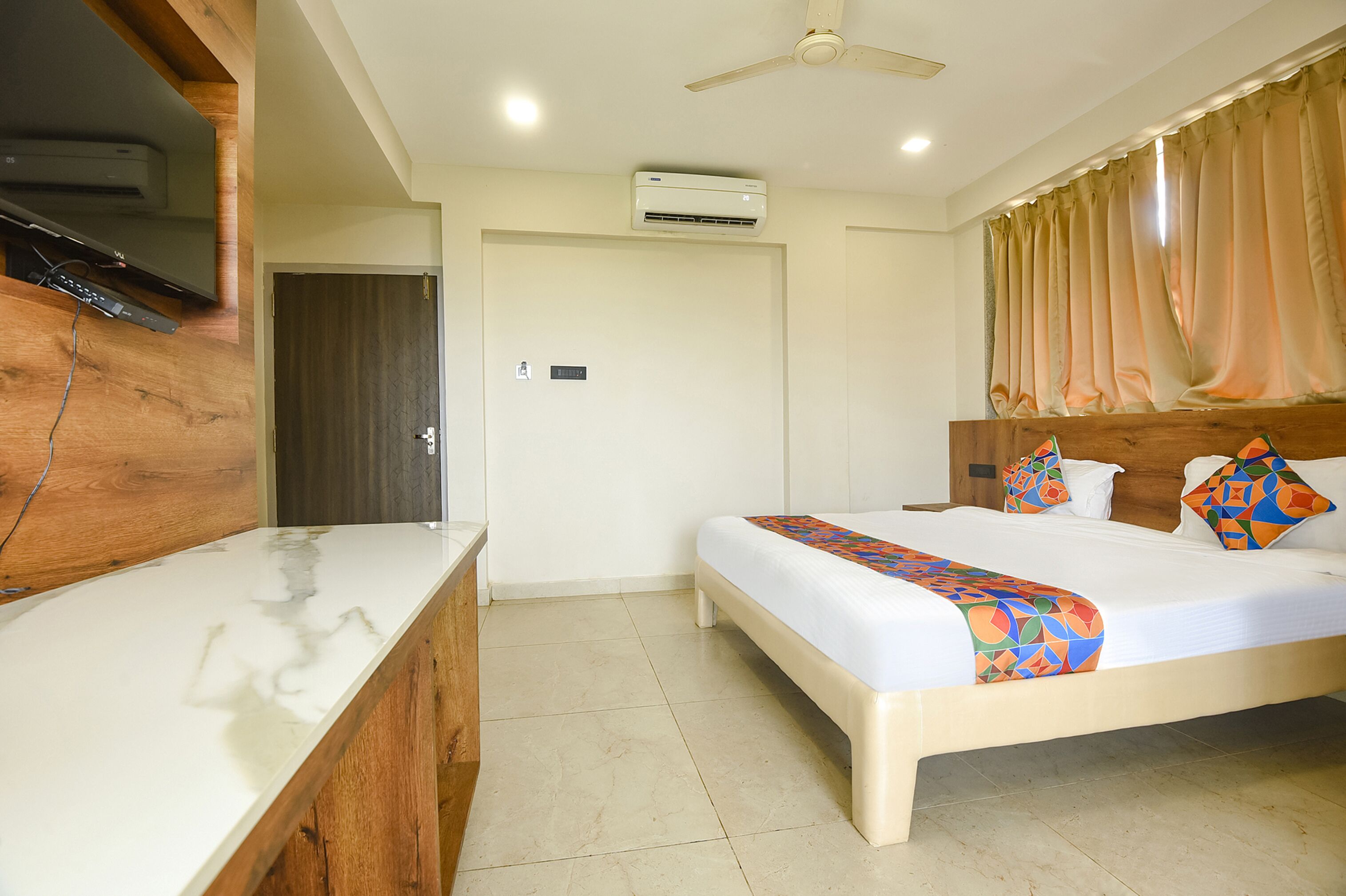 A hotel room with a bed, a desk, an air conditioning unit, and a ceiling fan.