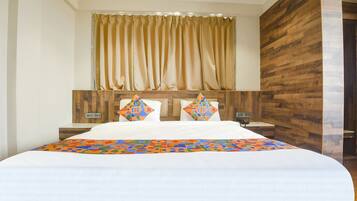 A hotel room with a large bed, a wooden headboard, a window with curtains, and a nightstand with a lamp.