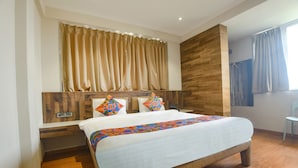 A hotel room with a large bed, wooden headboard, curtains, and a small table. - Fabhotel Avasa Grand (Panaji)